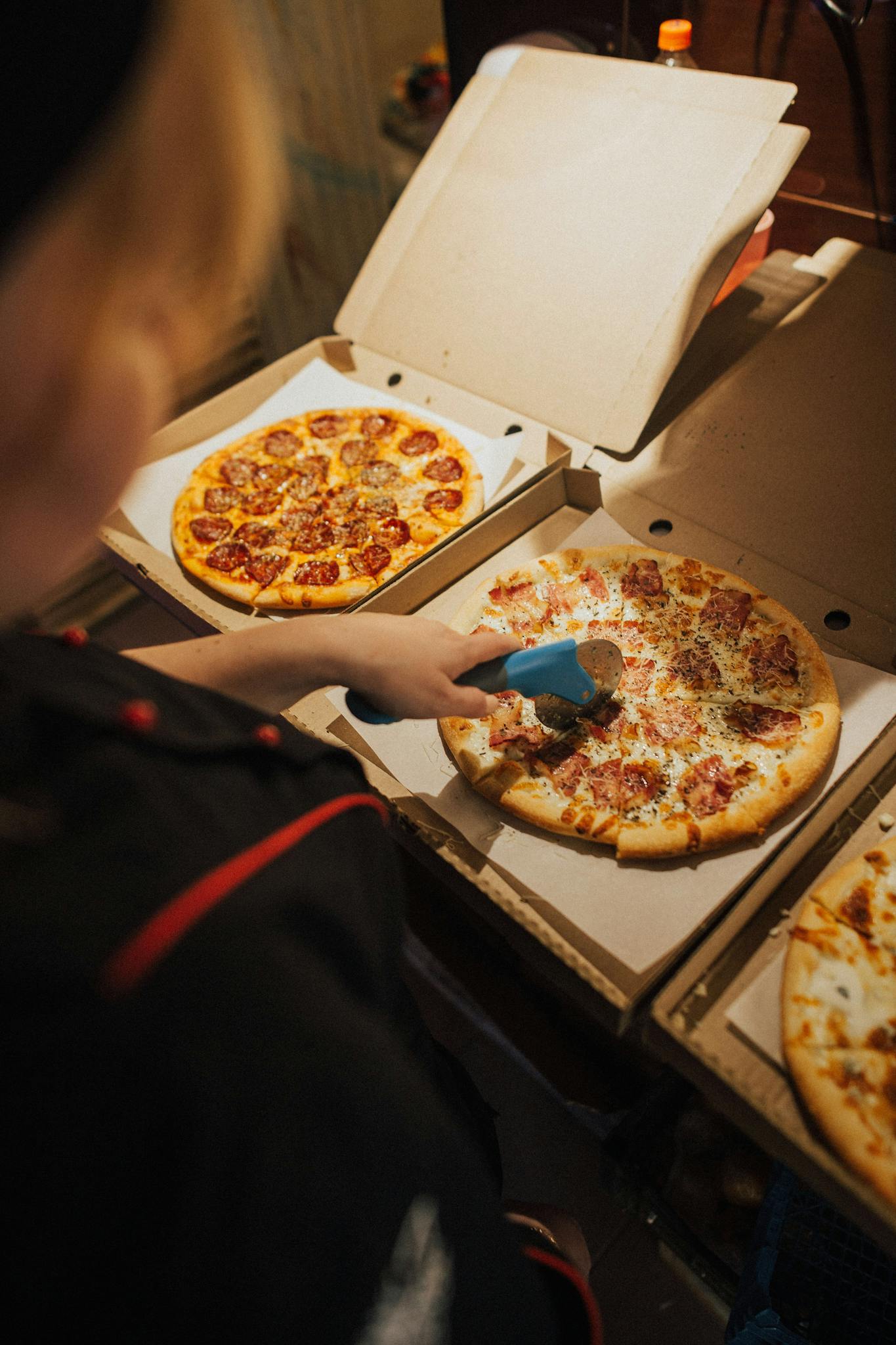 A person using a pizza cutter to slice pizzas inside open boxes, ready for delivery.