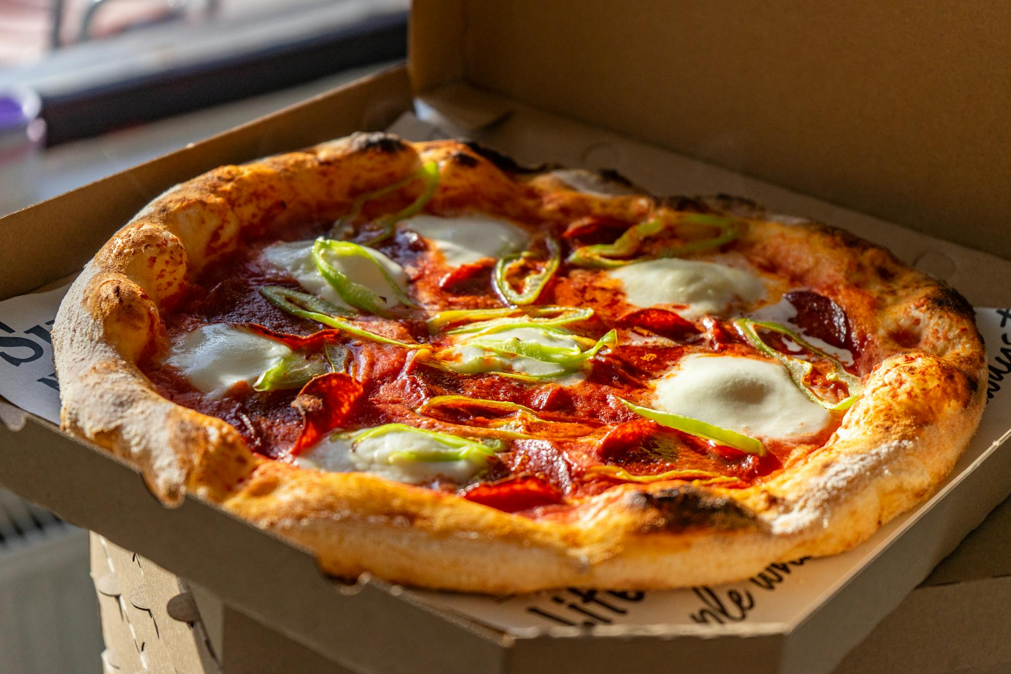 Tasty Neapolitan pizza with fresh ingredients in a cardboard box, perfect for takeout.