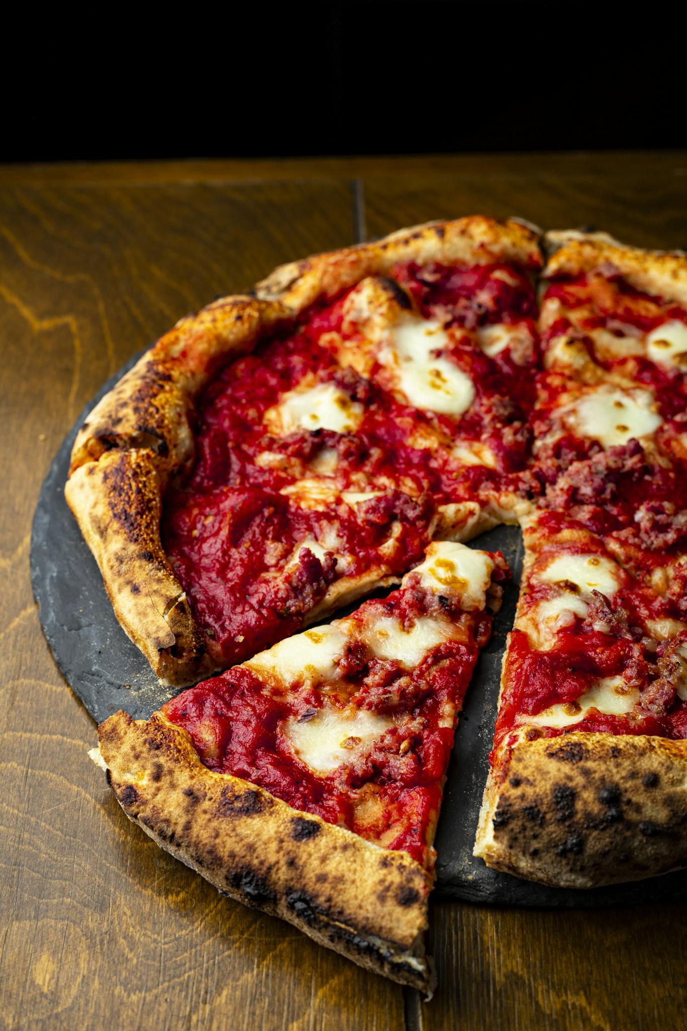 Tasty Neapolitan pizza with melted cheese and sausage toppings on a rustic slate platter.